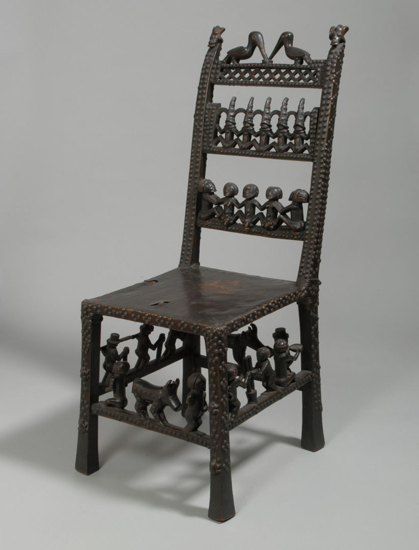 A dark wood African side chair decorated with seated figures and animals on the chair back, and on the rungs between the legs 
